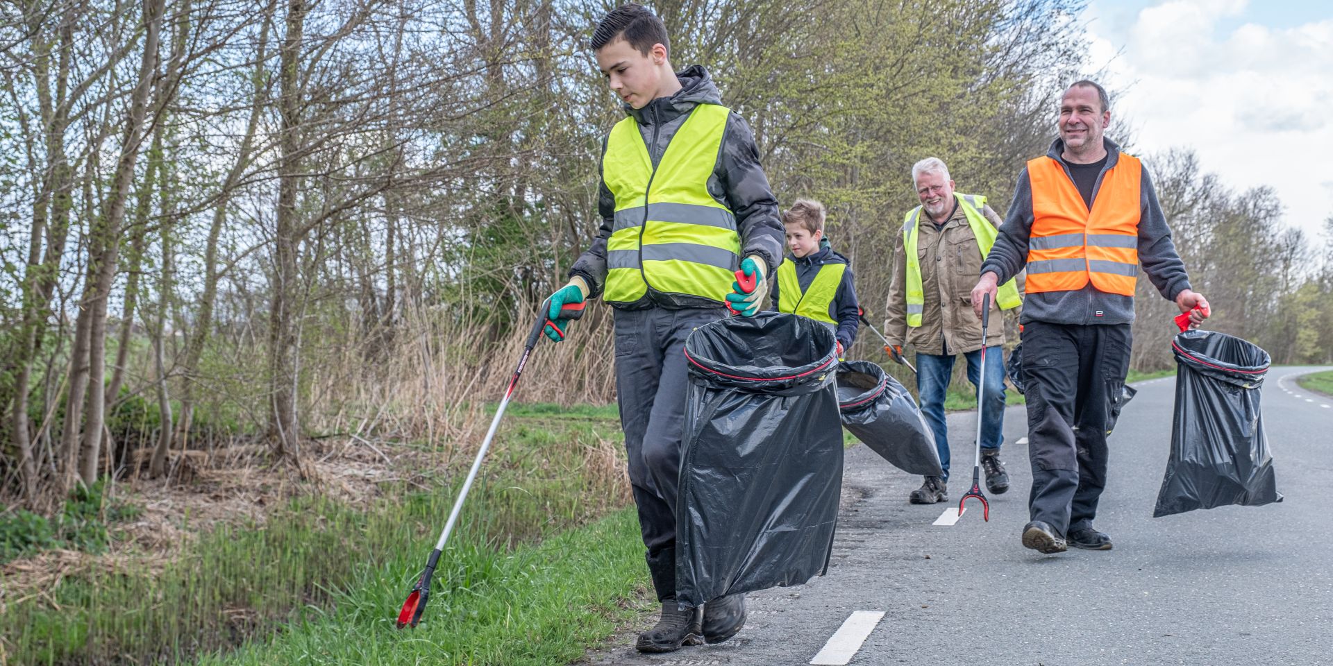 Vier mensen ruimen afval op, langs de kant van de weg.